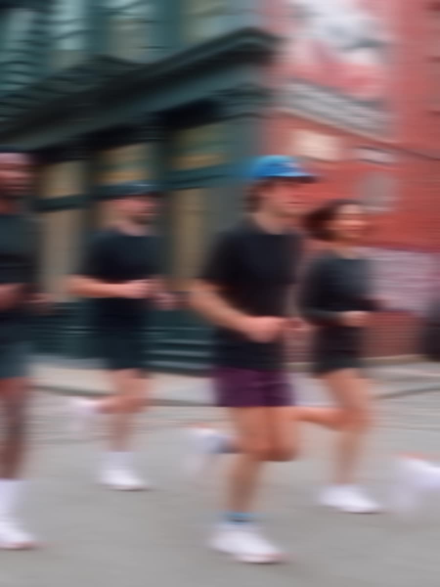 Five runners crossing a city street past a red brick corner building, motion-blurred.